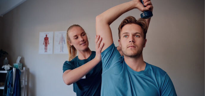 An exercise physiologist helping a patient lift a weight above their head